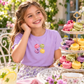 Sfeerbeeld met de kleine Macaronmoment-applicatie als bescheiden groep op een lila kindershirt, naast een etagère met macarons.