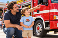 Sfeerbeeld: peuter met kleine Brandweerpret-applicatie op zijn shirt bekijkt samen met zijn vader een brandweerwagen.
