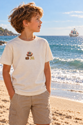 Sfeerbeeld: jongetje op het strand met een kleine piratenapplicatie op zijn shirt en een piratenschip in de verte